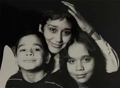 Black and white photo with Reyes-Jimenez in center, hand touching top of head, young boy to her left and young girl to her right.