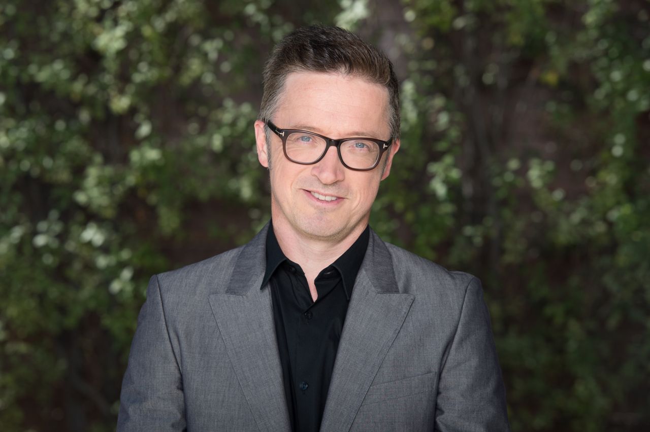 A picture of Rick Adams wearing a grey jacket in front of a background of greenery.