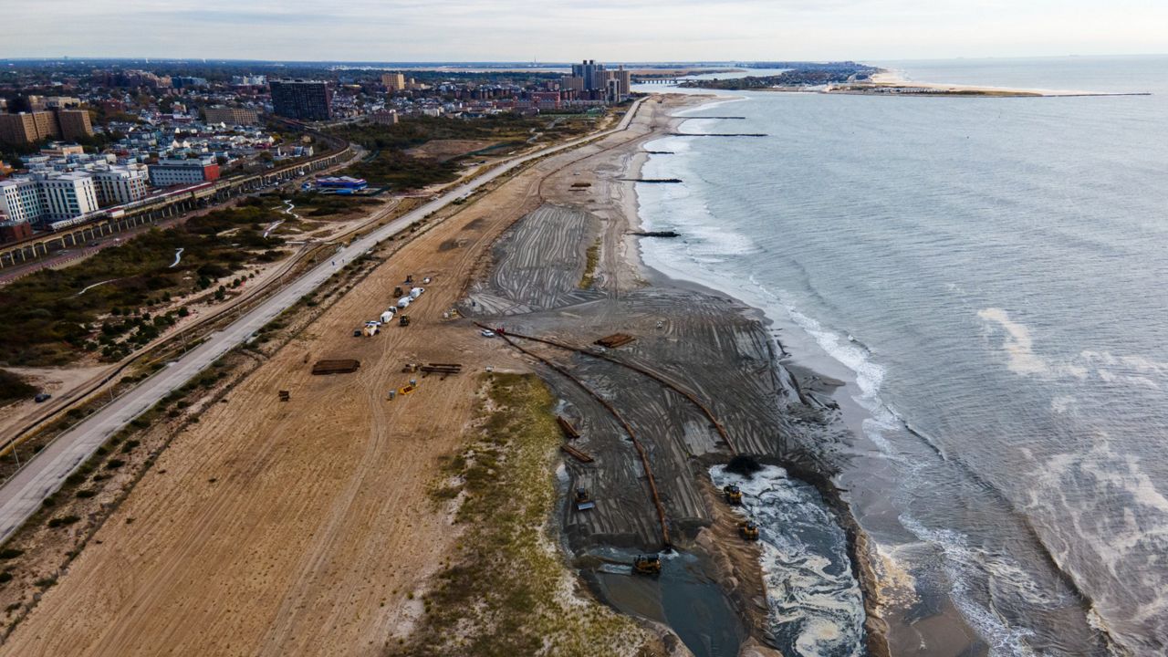 In an aerial photograph, large machines pump sand from the edge of the ocean onto the beach of the Rockaways. 