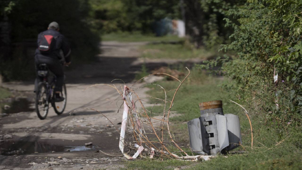 A man cycles past part of a rocket that sits wedged in the ground at a residential area in Sloviansk, Ukraine, Monday, Sept. 5, 2022. (AP Photo/Leo Correa)