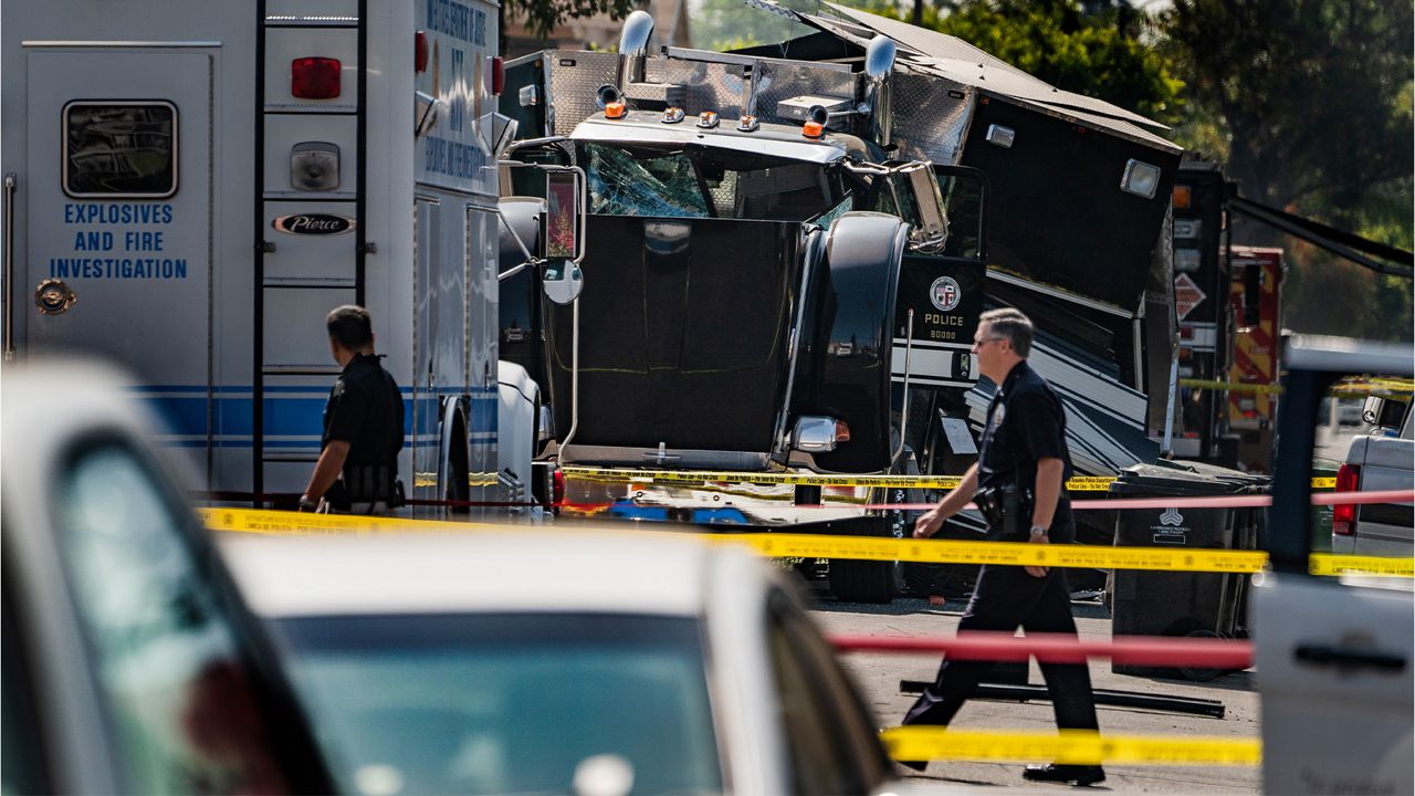 In this July 1, 2021, file photo, police officers walk past the remains of an armored Los Angeles Police Department tractor-trailer, after illegal fireworks seized at a South LA home exploded. (AP Photo/Damian Dovarganes)