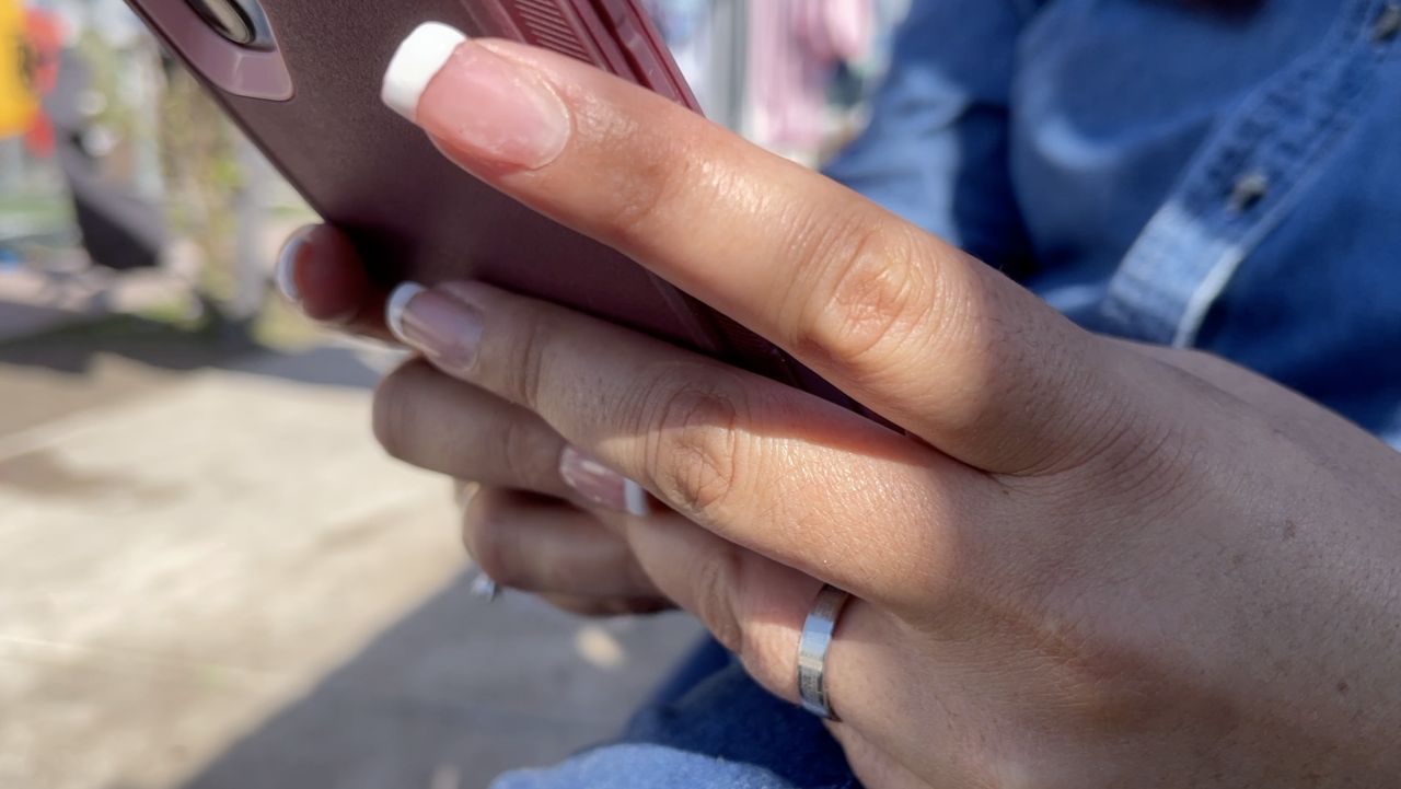 An asylum-seeker checks her phone on the Mexican side of the U.S.-Mexico border in this image from December 2021. (Spectrum News 1/John Salazar)
