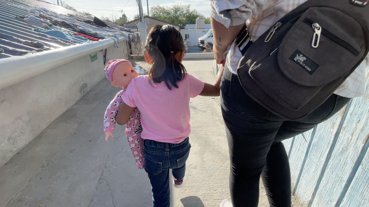 An asylum-seeker walks with a child on the Mexican side of the U.S.-Mexico border in this image from December 2021. (Spectrum News 1/John Salazar)
