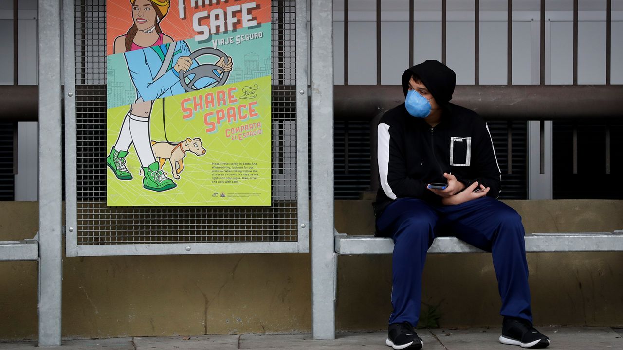 A bus rider wearing a face mask waits at a stop Monday, March 16, 2020, in Santa Ana, Calif. Millions of California's oldest and youngest residents stayed home Monday as officials took increasingly strident steps to separate people and contain the spread of the coronavirus. According to the World Health Organization, most people recover in about two to six weeks, depending on the severity of the illness. (AP Photo/Chris Carlson)