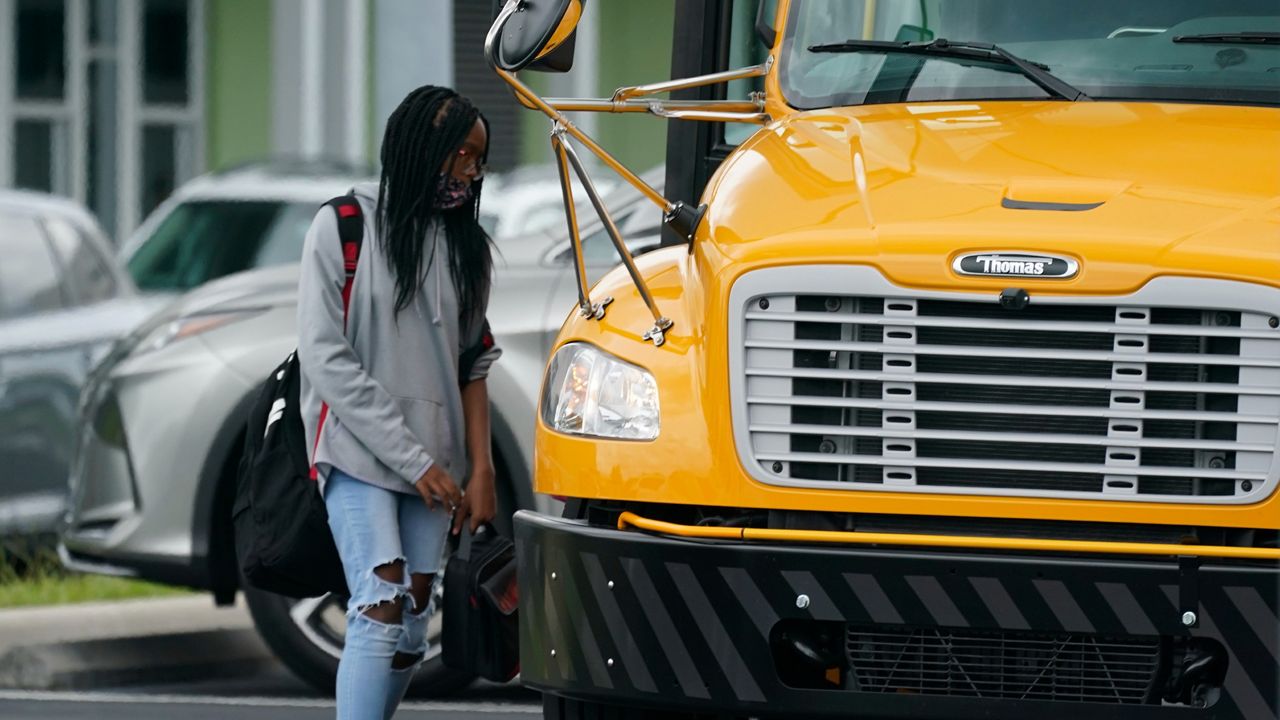 Student wearing mask next to bus. (AP Images)