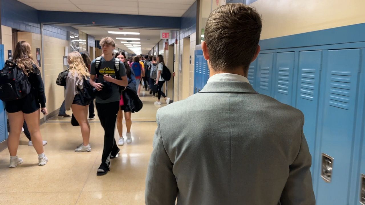 high school student, in a gray blazer, walks down a high school hallway