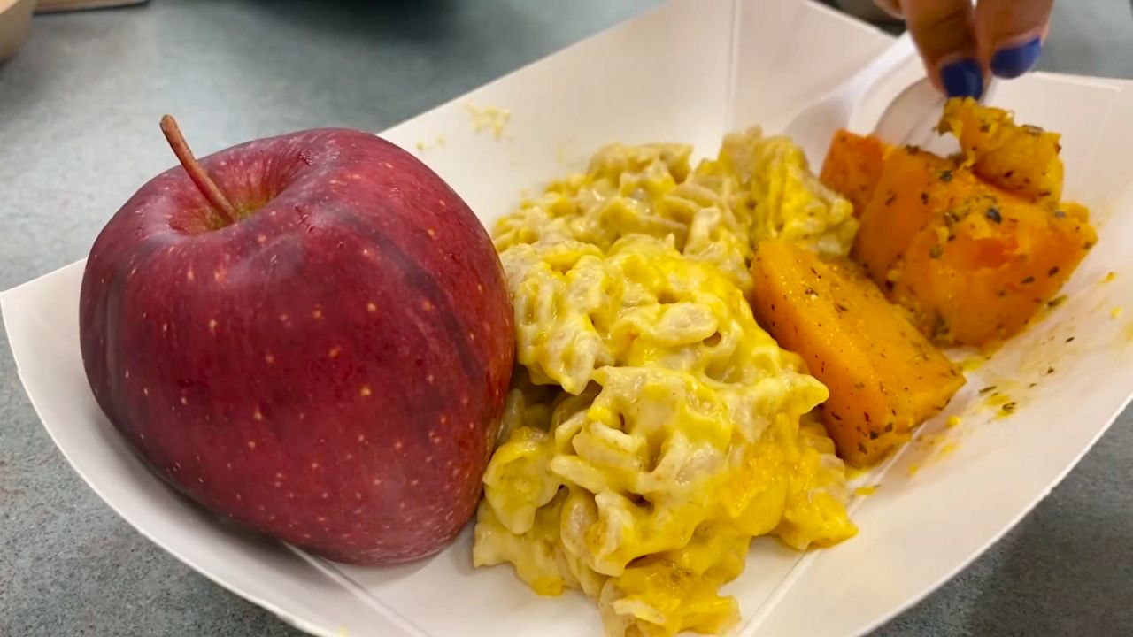 an apple, macaroni and cheese and sweet potato in a paper dish, on a black tabletop