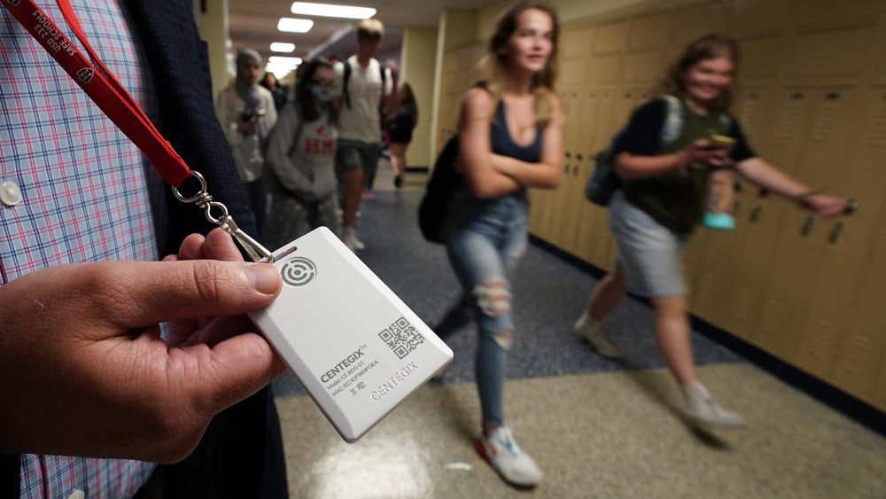 Brent Kiger, Olathe Public Schools' director of safety service, displays a panic-alert button while students at Olathe South High School rush between classes Friday, Aug. 19, 2022, in Olathe, Kan. The district introduced the buttons, which allow staff to trigger a lockdown that will be announced with flashing strobe lights, a takeover of staff computers and a prerecorded intercom announcement, at the start of this school year as part of $2.1 million plan to make district schools more secure. (AP Photo/Charlie Riedel)