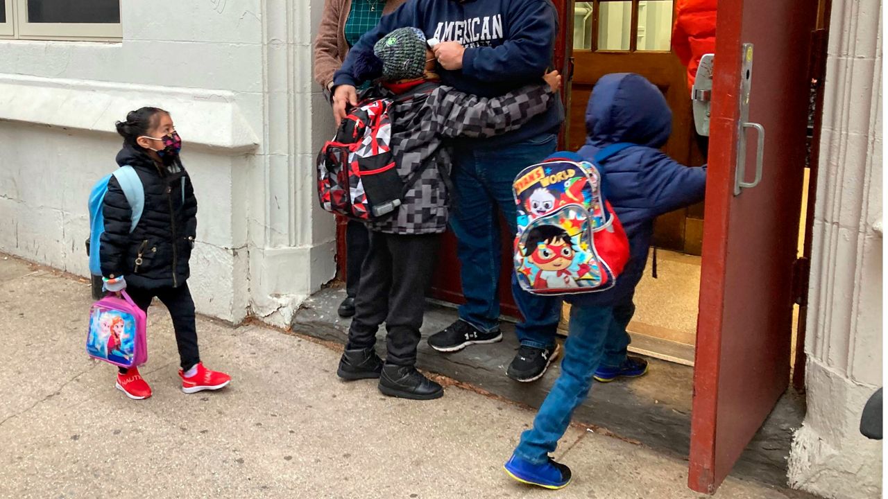John Marro, the dean of students at P.S. 347, The American Sign Language and English Lower School, in New York, takes students' temperatures as they arrive on the first day after the holiday break, Monday, Jan. 3, 2022.