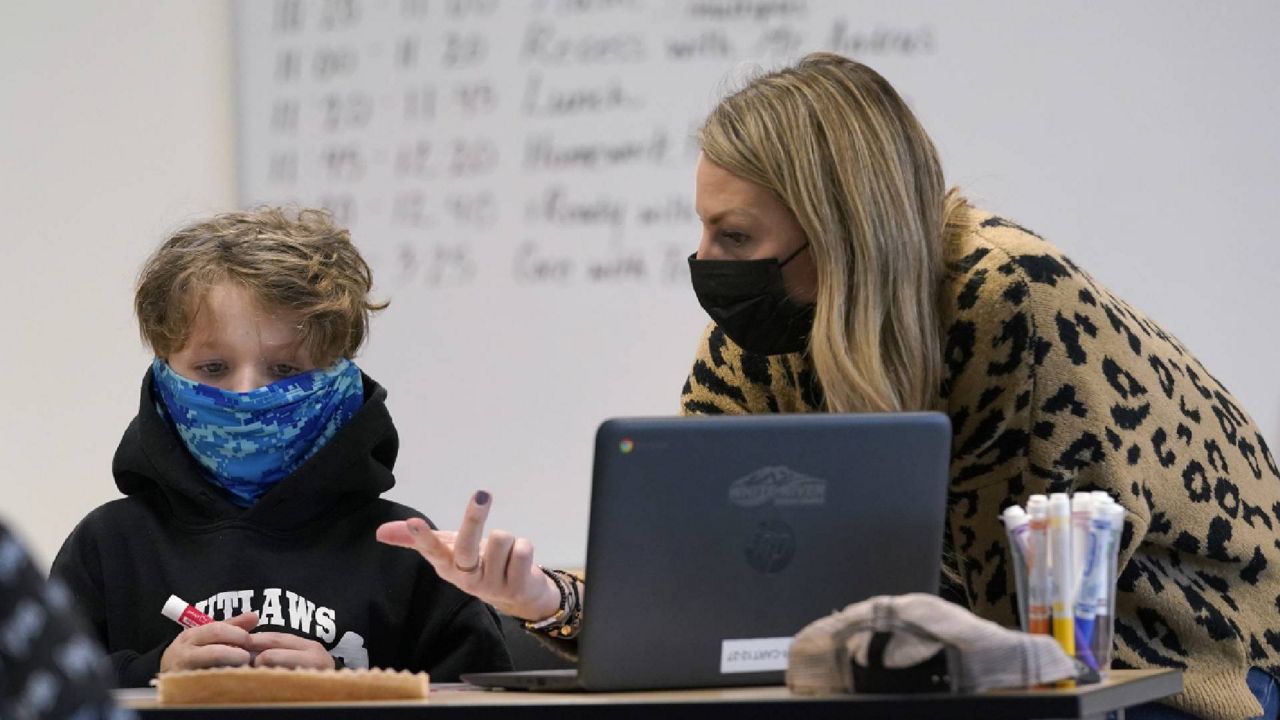 A masked teacher works with a student on a math problem in a fourth-grade classroom in Washington Tuesday. The school has had some students in classrooms for in-person learning since September of 2020, but other students who attend the school are still learning remotely. (AP Photo/Ted S. Warren)