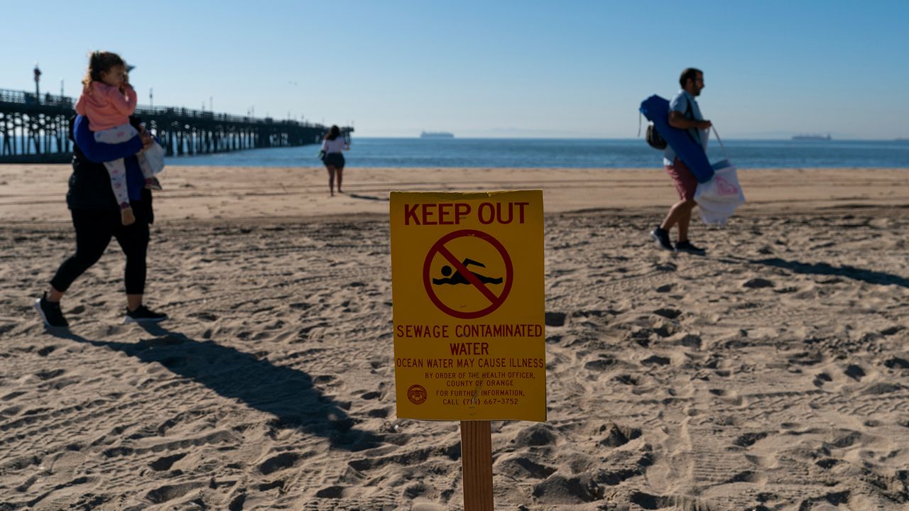 Visitors walk along the sand near a beach closure sign in Seal Beach, Calif., Monday, Jan. 3, 2022. (AP Photo/Jae C. Hong)