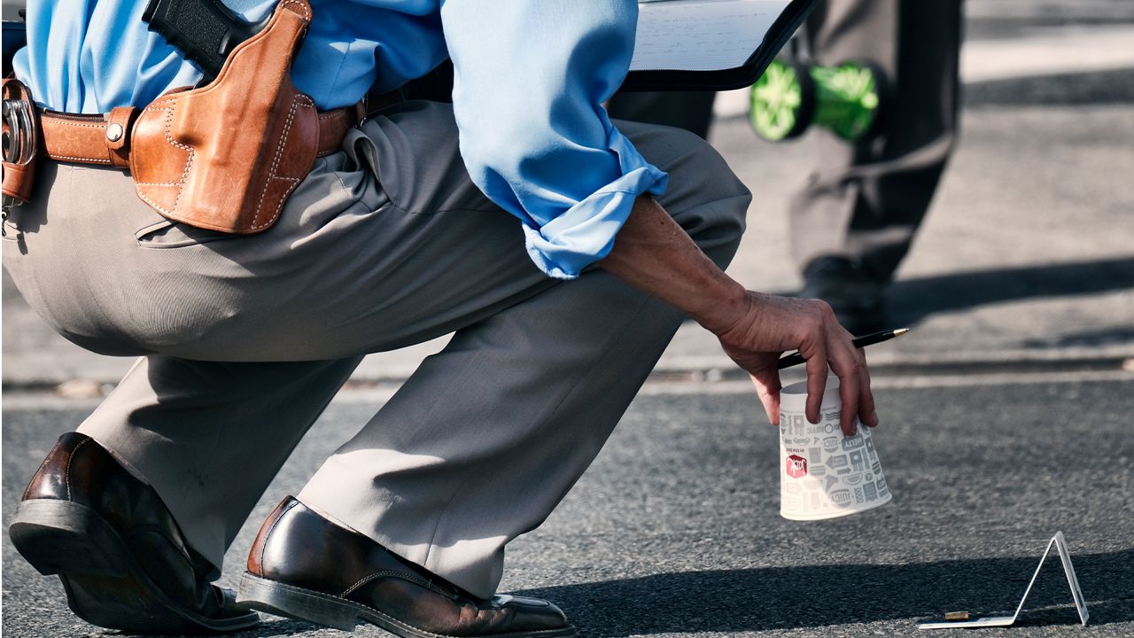 A Los Angeles Police Detective lifts a Jack in the Box drinking cup marking a shell casing during an investigation at the scene of a shooting in the Van Nuys section of Los Angeles on Thursday, Sept. 20, 2018. (AP Photo/Richard Vogel)