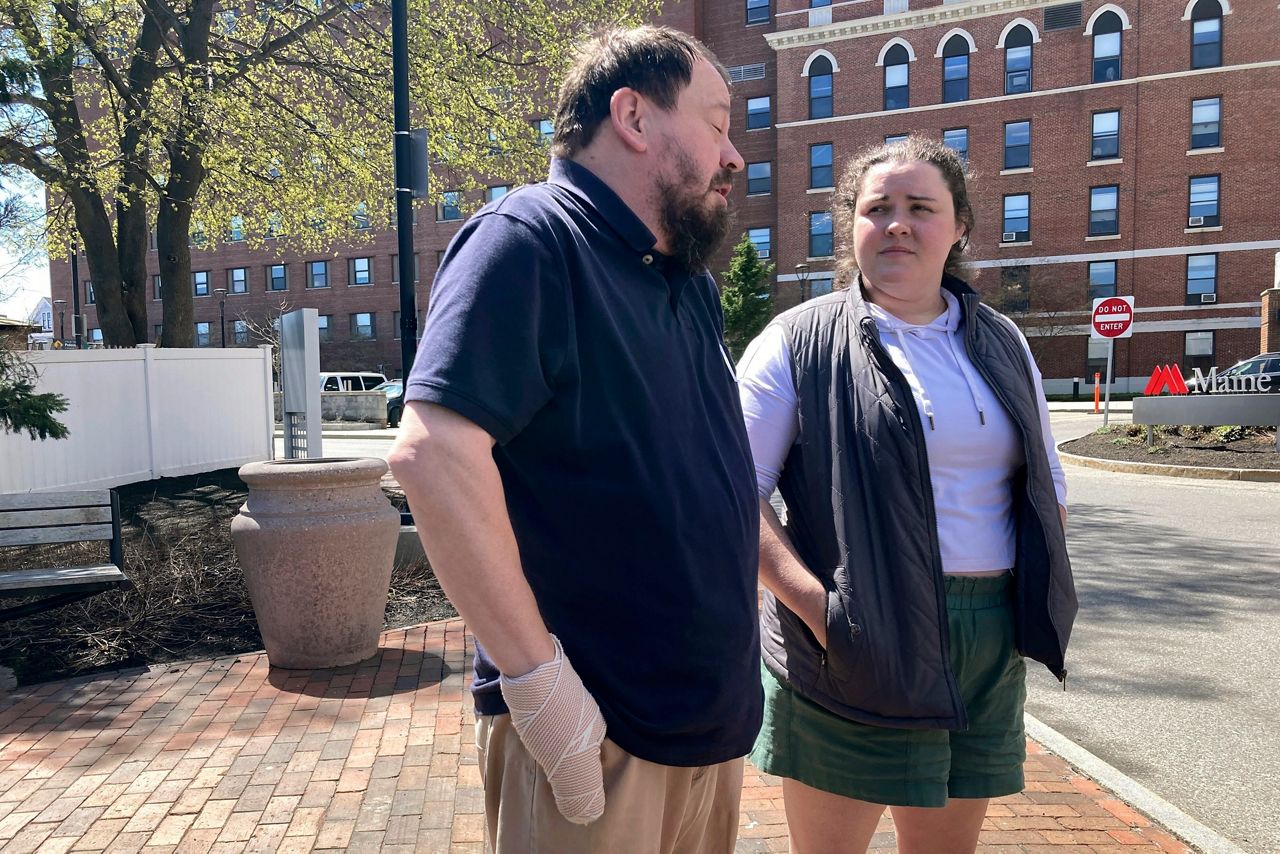 Sean Halsey, left, who was injured along with his children (not shown) in a shooting in Maine last week, speaks at a news conference outside Maine Medical Center in Portland, Maine, Friday, April 28, as family friend Haley Murphy, right, listens on. (AP Photo/Patrick Whittle)