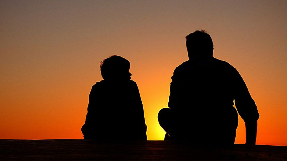A parent and child appear in silhouette in this stock image. (Pixabay) 