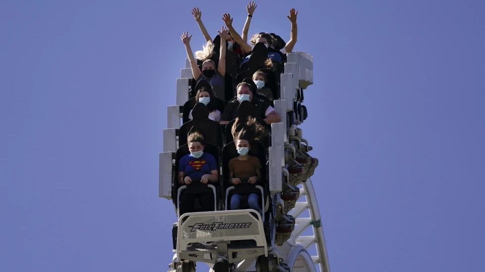 Visitors wearing masks ride on a roller coaster at Six Flags Magic Mountain on its first day of reopening to members and pass holders in Valencia, Calif., on April 1, 2021. Cedar Fair and Six Flags Entertainment Corp. are merging, creating an expansive amusement park operator with operations spread across 17 states and three countries. (AP Photo/Jae C. Hong, File)