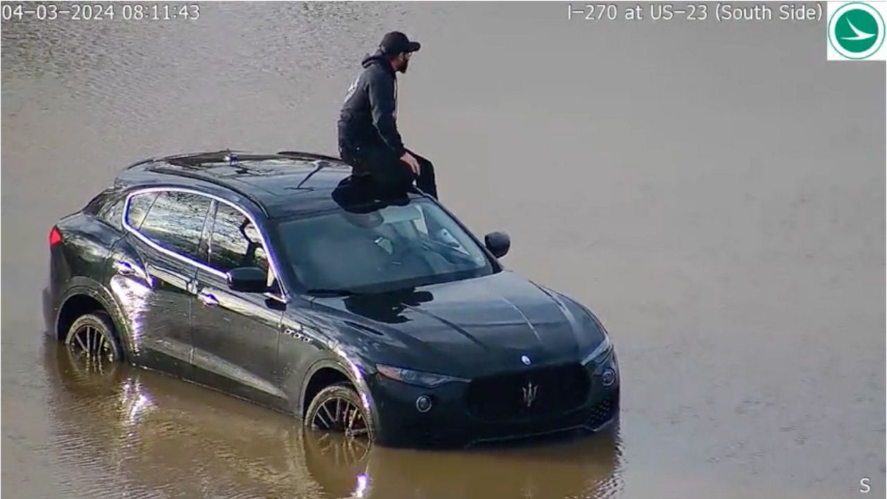 A man sits on top of his car after driving onto flooded U.S. 23 at I-270 on the south side of Columbus.