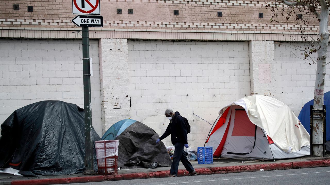A man covers his face with a mask as he walks past tents on skid row, in Los Angeles on March 20, 2020. (AP Photo/Marcio Jose Sanchez)