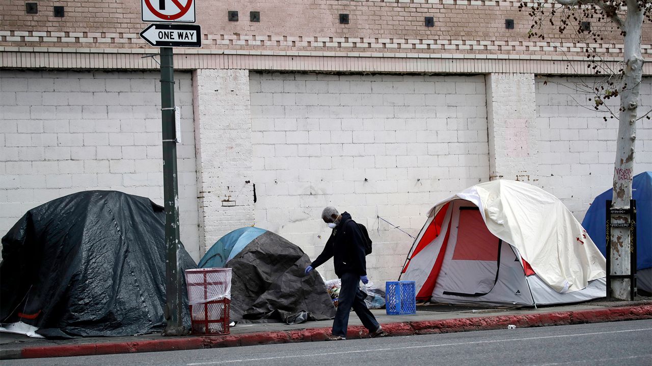 A man covers his face with a mask as he walks past tents on skid row, in Los Angeles on March 20, 2020. (AP Photo/Marcio Jose Sanchez)
