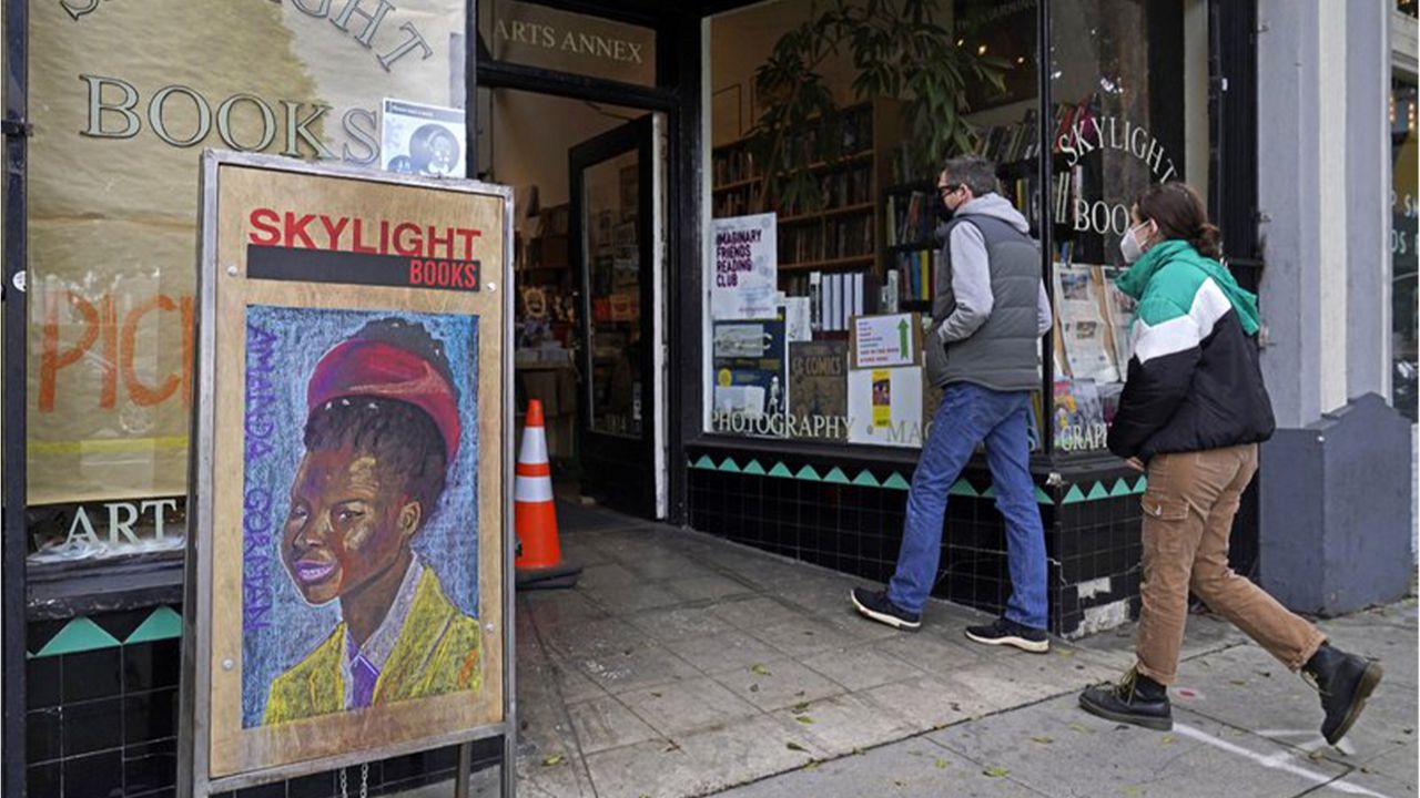 Eric and Tess from Pasadena, Calif., enter the Skylight Book store, decorated with a poster of American poet Amanda Gorman, in Los Feliz neighborhood of Los Angeles Monday, Jan. 25, 2021.  (AP Photo/Damian Dovarganes)