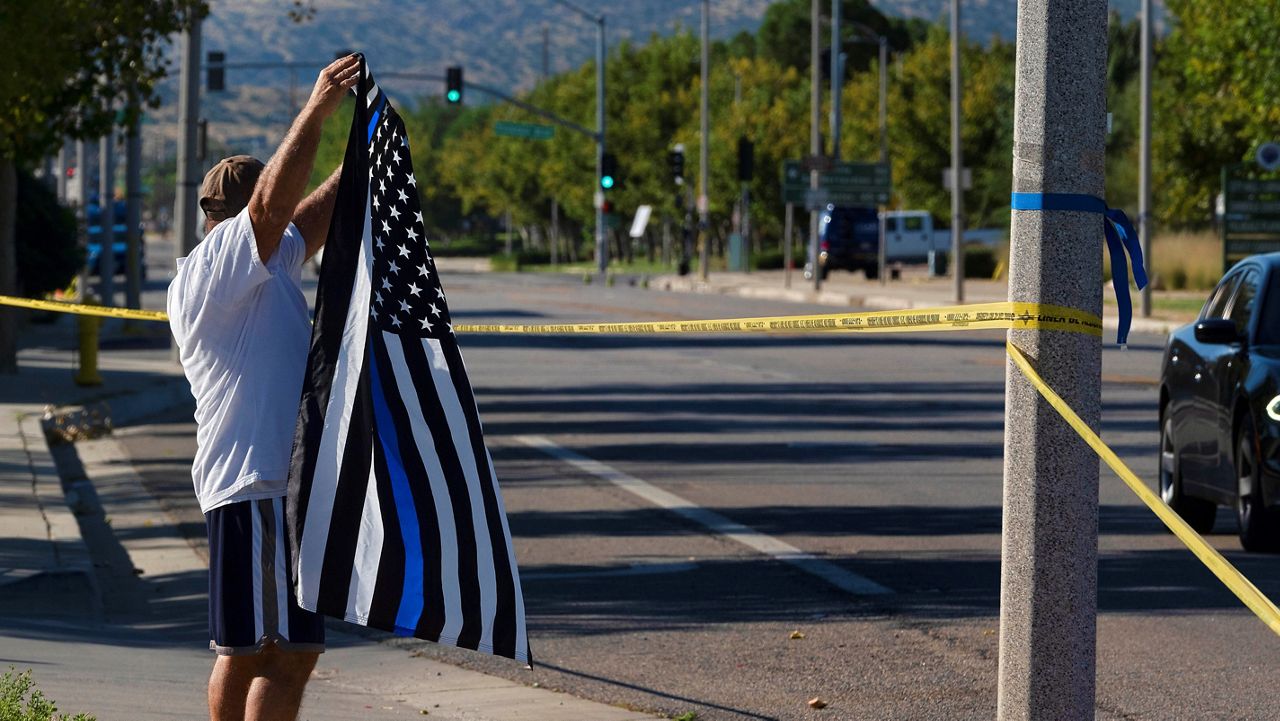 A local resident waves a Thin Blue Line flag in support of a deputy who was shot while in his patrol car in Palmdale, Calif. on Sunday, Sept. 17, 2023. A sheriff's department deputy has died after he was shot in his patrol car by an unknown assailant on Saturday, and an investigation is underway. (AP Photo/Richard Vogel)