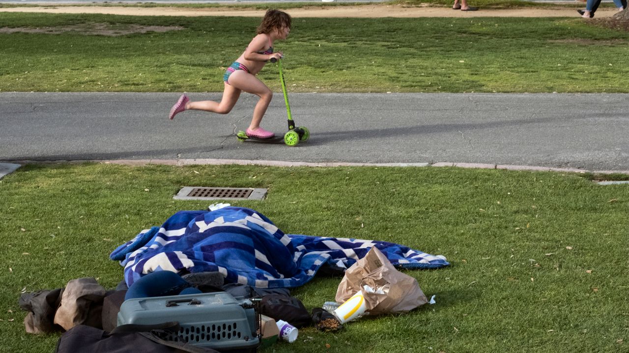 In this Monday, June 3, 2019 photo a child rides her scooter past a homeless person covered under a blanket in Santa Monica, Calif. (AP Photo/Richard Vogel)