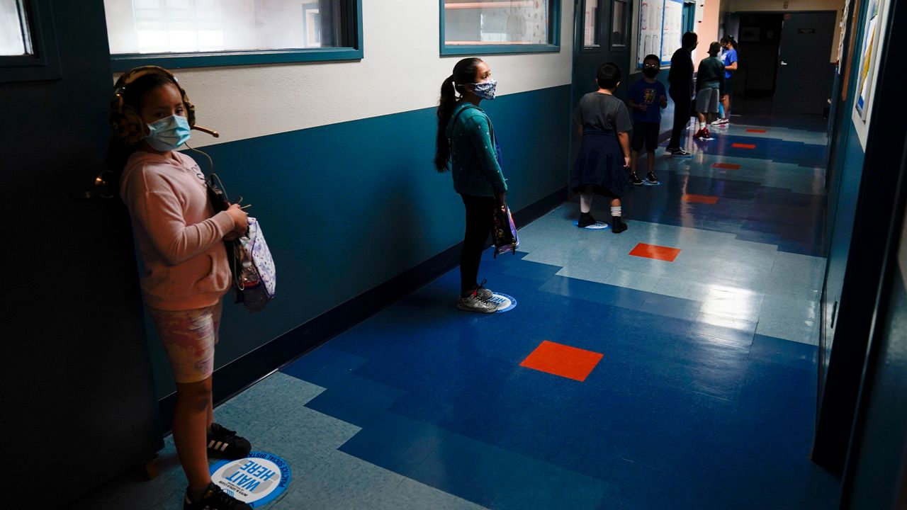 In this Aug. 26, 2020, file photo, Los Angeles Unified School District students stand in a hallway socially distance during a lunch break at Boys & Girls Club of Hollywood in Los Angeles.  (AP Photo/Jae C. Hong, File)