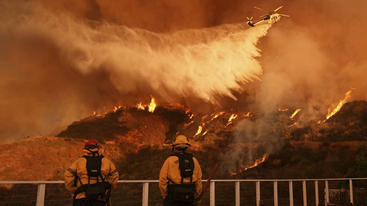 Firefighters watch as water is dropped on the Palisades Fire in Mandeville Canyon Saturday, Jan. 11, 2025, in Los Angeles. (AP Photo/Jae C. Hong)