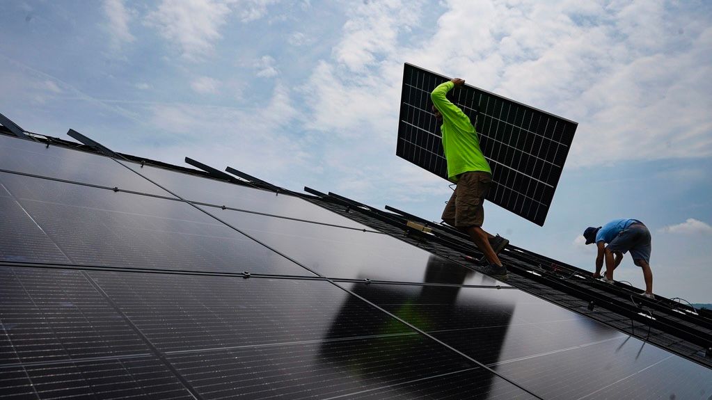 Nicholas Hartnett, owner of Pure Power Solar, carries a panel as he and Brian Hoeppner, right, install a solar array on the roof of a home in Frankfort, Ky., Monday, July 17, 2023. 