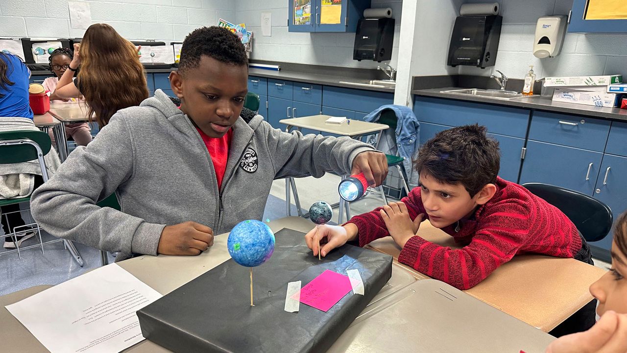 Alex Impion, 12, shines a flashlight on a model moon held by Necmeddin Aljabri, 8, at Riverside Elementary School in Cleveland on March 14, 2024. The two were learning about the upcoming total solar eclipse, a topic that has challenged and inspired teachers in and near the eclipse's path. (AP Photo/Carolyn Thompson)