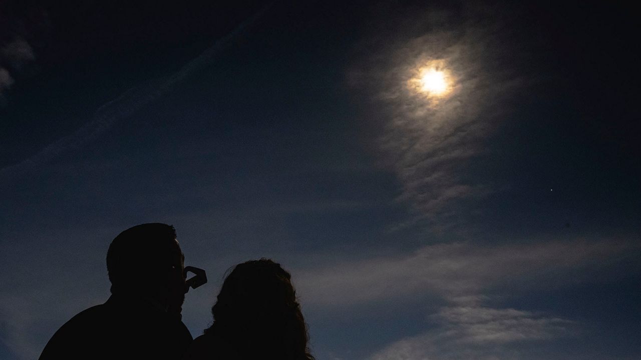 A newly wed couple looks up at a total solar eclipse during a mass wedding ceremony at Trenton Community Park, Monday, April 8, 2024, in Trenton, Ohio. (AP Photo/Jon Cherry)