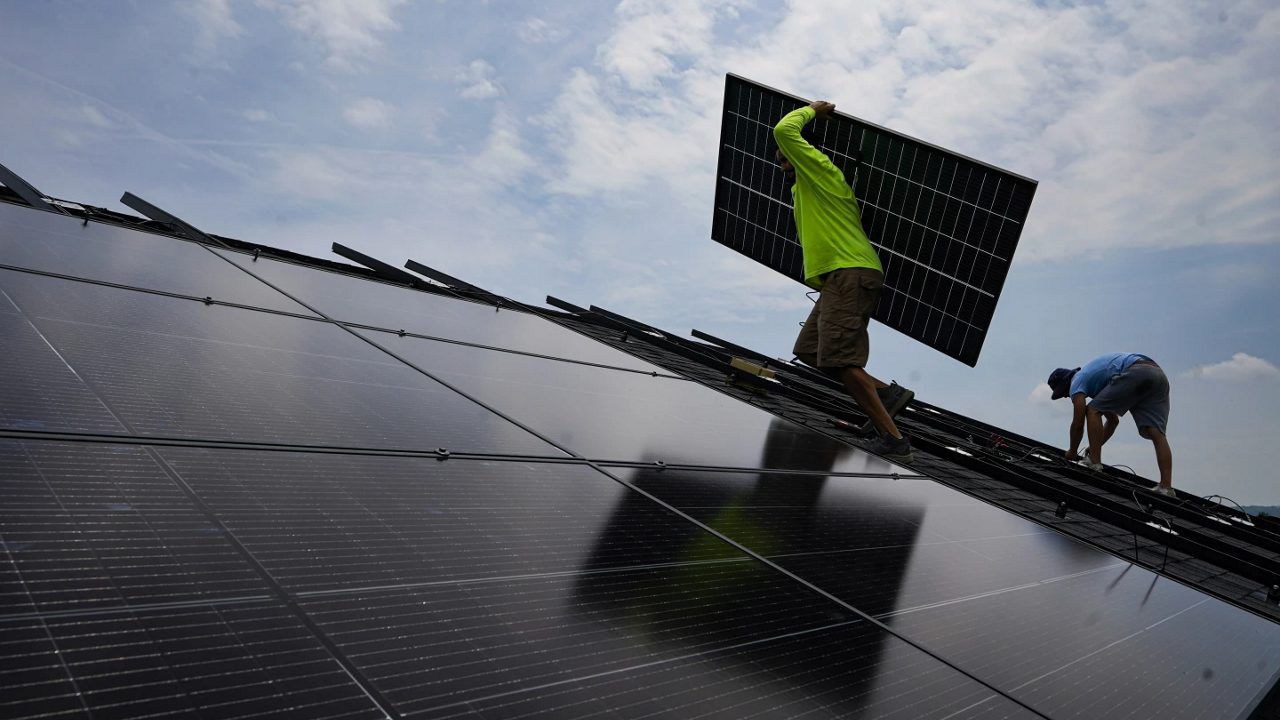 Nicholas Hartnett, owner of Pure Power Solar, carries a panel as he and Brian Hoeppner, right, install a solar array on the roof of a home in Frankfort, Ky., July 17, 2023. A business group that advocates for clean energy says at least $86 billion in investments have been announced, with the biggest likely job gains in electric vehicles, battery storage and solar energy. (AP Photo/Michael Conroy, File)