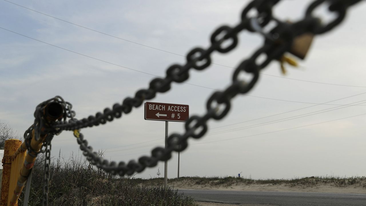 A lock and chain block an access point to the beach Saturday, March 21, 2020, in South Padre Island, Texas. (AP Photo/Eric Gay)