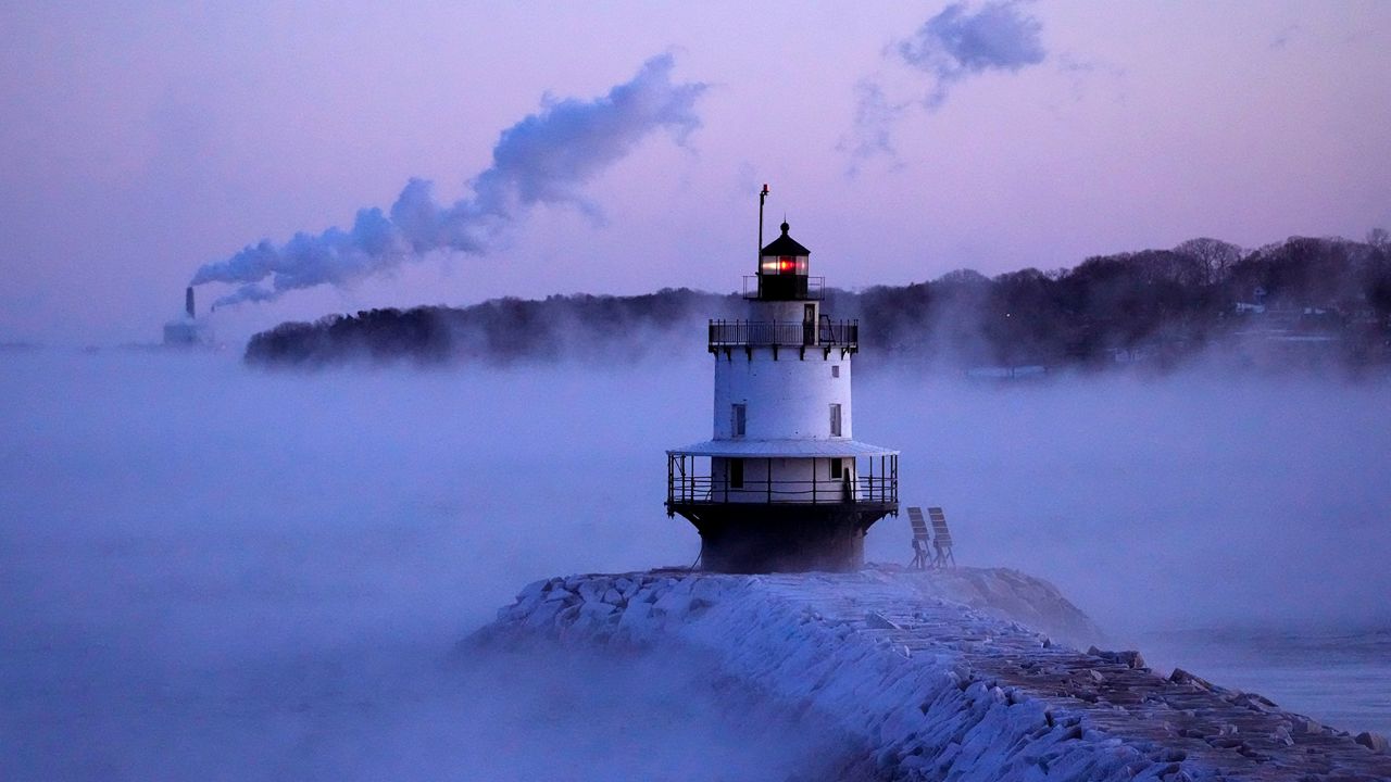 Spring Point Ledge Light is surrounded by arctic sea smoke while emissions from the Wyman Power plant, background, are blown horizontal by the fierce wind, Saturday, Feb. 4, 2023, in South Portland, Maine. The morning temperature was about -10 degrees Fahrenheit. (AP Photo/Robert F. Bukaty)