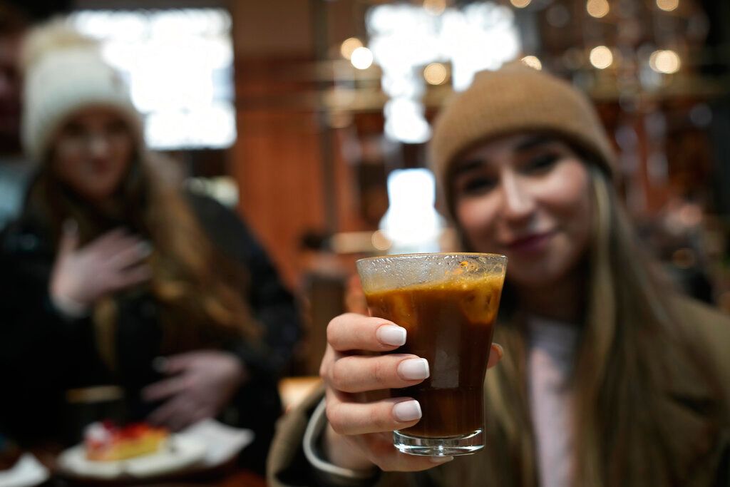 Kaya Cupial, right, shows her Oleato Iced Cortado coffee at the Starbucks coffee shop in Milan, Italy, Monday, Feb. 27, 2023. Putting olive oil in coffee is hardly a tradition in Italy, but that didn't stop Starbucks founder and CEO Howard Schultz from launching a series of beverages doing just that in Milan, the city that inspired his coffee house empire. (AP Photo/Antonio Calanni)