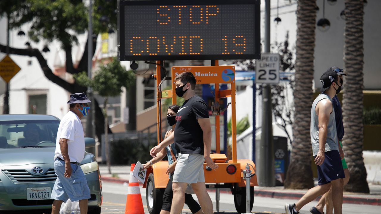 Pedestrians wear masks as they cross a street amid the coronavirus pandemic Sunday, July 12, 2020, in Santa Monica, Calif. A heat wave has brought crowds to California's beaches as the state grappled with a spike in coronavirus infections and hospitalizations. (AP Photo/Marcio Jose Sanchez)