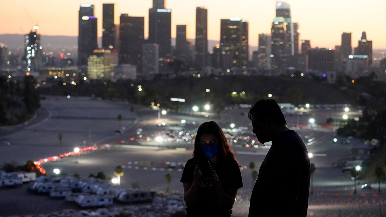 Visitors wear masks at a lookout point over at a COVID-19 vaccination site at Dodger Stadium Friday, Jan. 15, 2021, in Los Angeles. (AP Photo/Marcio Jose Sanchez)
