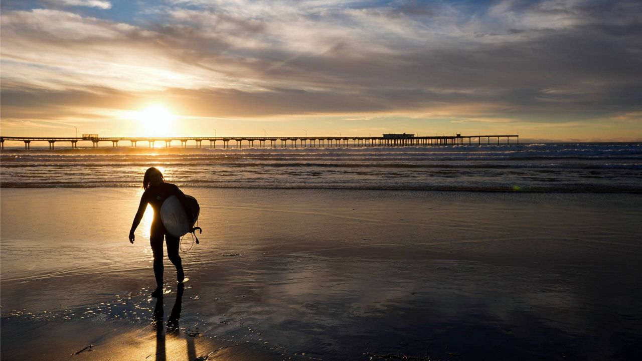 A surfer walks in front of the Ocean Beach pier as the sun sets Tuesday in San Diego. (AP Photo/Gregory Bull)