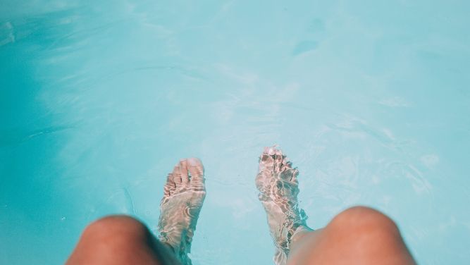 A person dips their legs into the swimming pool.