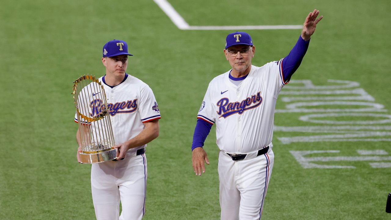 Texas Rangers relief pitcher Josh Sborz, left, and manager Bruce Bochy, right, walk the Commissioner's Trophy onto the field before the team's baseball game against the Chicago Cubs, Thursday, March 28, 2024 in Arlington, Texas. (AP Photo/Gareth Patterson)