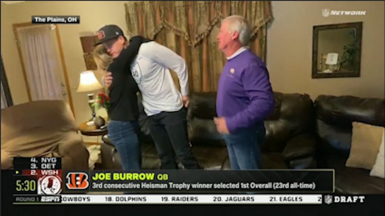 Joe Burrow in his living room with his mom hugging him and his dad with a purple shirt standing next to them