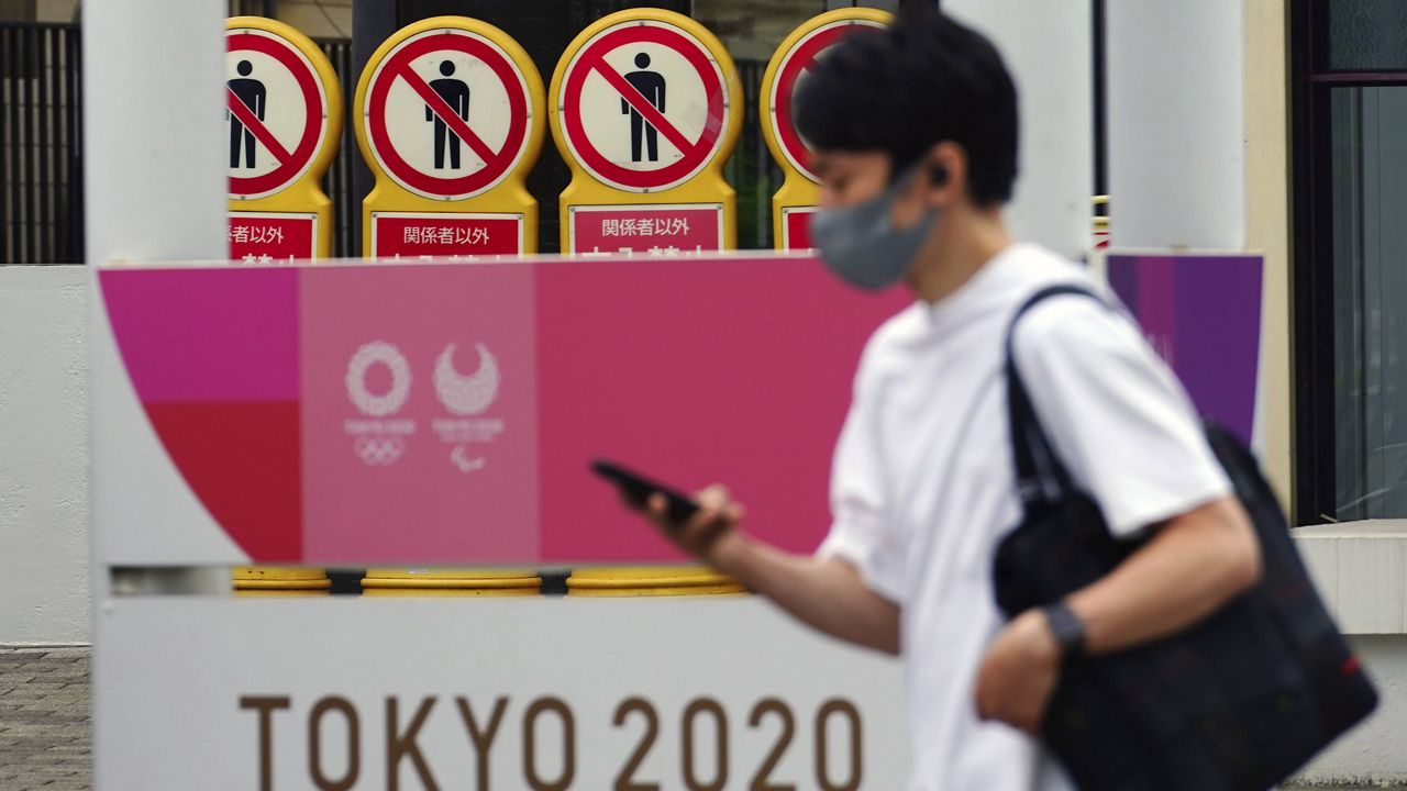 A man wearing a protective mask walks past a banner for the Tokyo 2020 Olympic and Paralympic Games on May 11, 2021, in Tokyo. (AP Photo/Eugene Hoshiko)