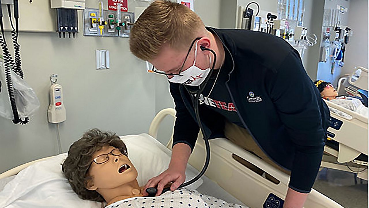 Student leaning over hospital bed checking the heartbeat of a practice dummy