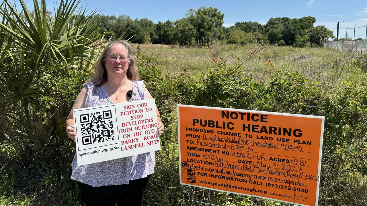 Susan Pritchard, head of the Twelve Oaks Civic Association, stands next to open land at the corner of Soccer Avenue and Armand Drive that developers want to build on. The land used to be the Barry Road Landfill, which was once filled with all sorts of waste. (Spectrum News/Dalia Dangerfield)