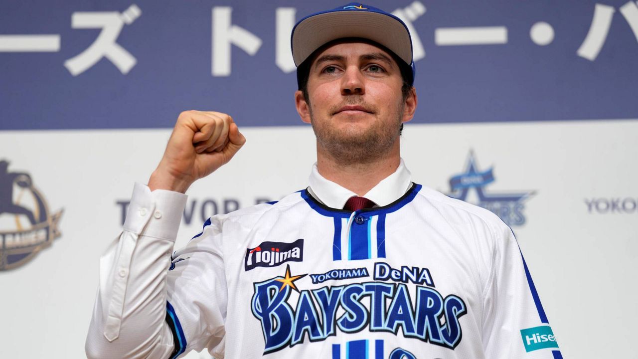 Trevor Bauer with his new uniform and cap of Yokohama DeNA BayStars poses for photographers during a photo session of the news conference Friday in Yokohama, near Tokyo. (AP Photo/Eugene Hoshiko)