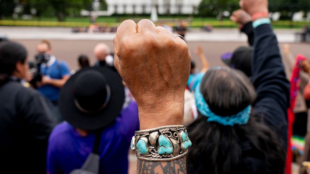 Wolf Ramerez of Houston, Texas, center, joins others with the Carrizo Comecrudo Tribe of Texas in holding up his fists as indigenous and environmental activists protest in front of the White House in Washington, Oct. 11, 2021. (AP Photo/Andrew Harnik 