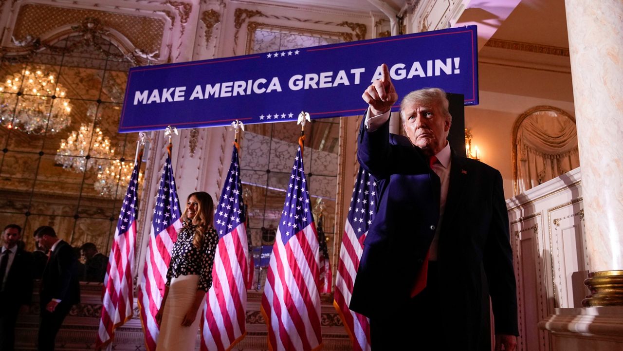 Donald Trump stands in front of a sign that says Make American Great Again