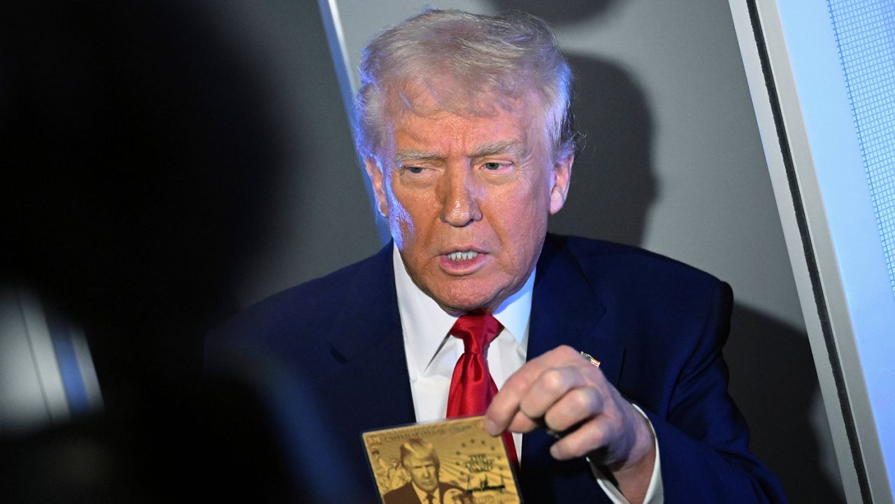 President Donald Trump holds up the $5 million gold card as he speaks to reporters while in flight on board Air Force One, en route to Miami, Thursday, April 3, 2025. (Pool via AP)