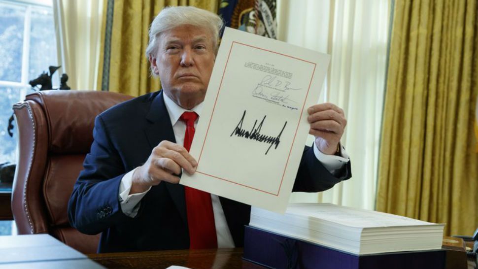 President Donald Trump shows off the tax bill after signing it in the Oval Office of the White House. (AP Photo/Evan Vucci)
