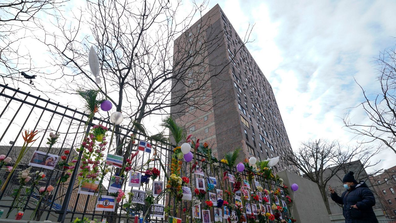 A memorial, with pictures and flowers, for the victims of an apartment building fire is displayed front of a tree, fence and an apartment building in the Bronx borough of New York, Thursday, Jan. 13, 2022.