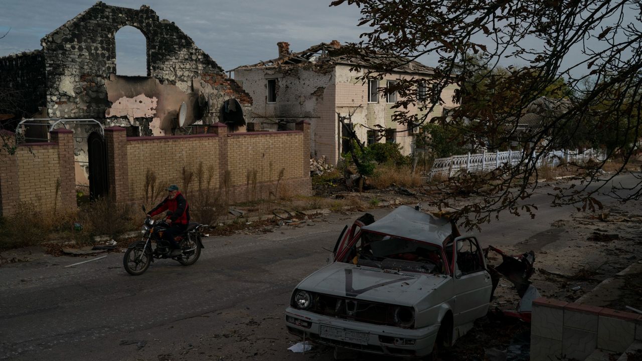 A man drives his motorcycle Wednesday past a destroyed car in the retaken village of Velyka Oleksandrivka, Ukraine. (AP Photo/Leo Correa)